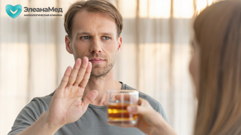 Мужчина жестом ладони отказывается от стакана с алкоголем